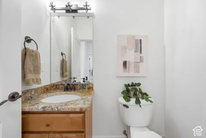 Wood-finish vanity cabinet with a stone countertop, undermount sink, three-light wall fixture, and wall-mounted mirror