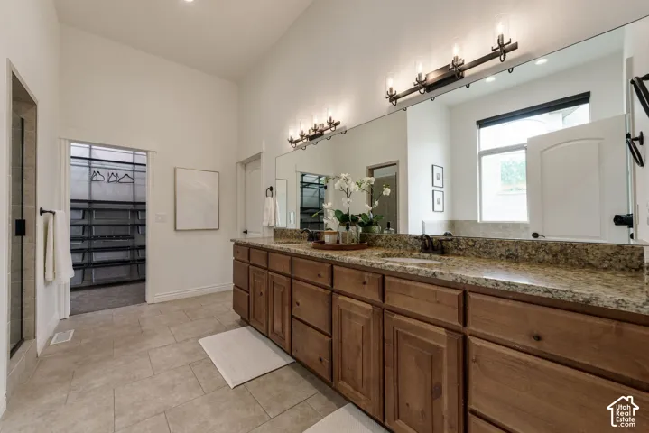 Double vanity featuring wood cabinetry, stone countertops with dual undermount sinks, full-width wall mirror, and metal wall-mounted light fixtures