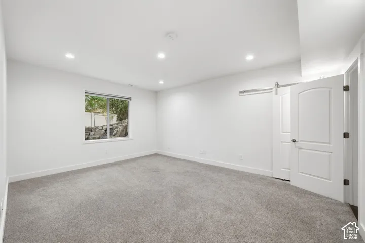 Neutral interior featuring recessed lighting, plush wall-to-wall carpeting, a sliding barn-style door, and a single-pane window with exterior rock landscaping