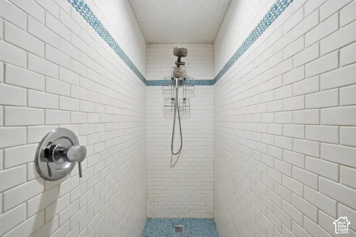 Walk-in shower featuring white subway tile walls, a blue glass mosaic tile inlay, blue circular floor tiling, and a chrome single-handle pressure-balance valve
