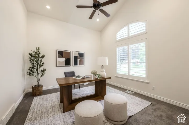 Vaulted ceilings featuring a central dark-finish ceiling fan, expansive arched window with plantation shutters, and neutral carpeting