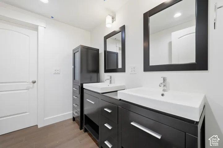 Double vanity with dark cabinetry, vessel sinks, chrome fixtures, matching framed mirrors, and wood-finish flooring