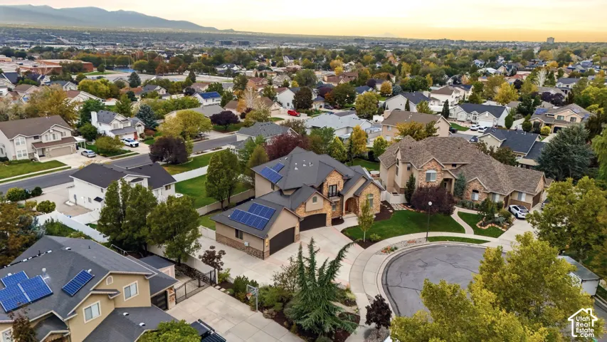 Aerial perspective of a multi-level stone and stucco residence featuring roof-mounted solar panels, a multi-car garage, and a concrete driveway situated within a cul-de-sac