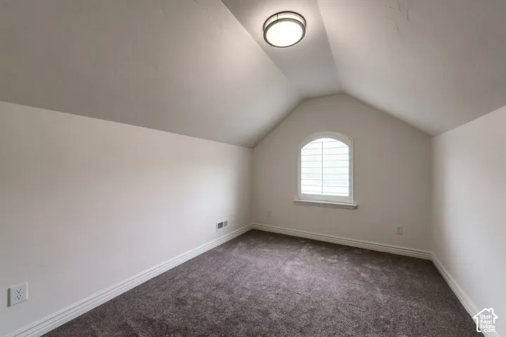 Vaulted ceiling, arched window with interior shutters, carpeted flooring, and flush-mount light fixture