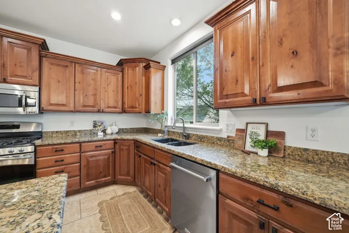 Kitchen featuring stained wood cabinetry, stone countertops, stainless steel appliances, a dual-basin undermount sink with a gooseneck faucet, and recessed lighting