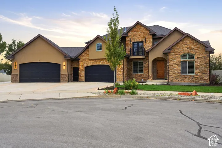 Multi-gabled exterior featuring stone veneer, stucco siding, a three-car garage, and a second-story balcony