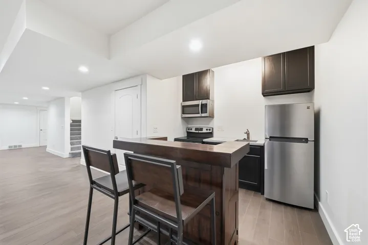 Kitchenette featuring a built-in dark wood breakfast bar, stainless steel appliances, dark cabinetry, recessed lighting, and wood-finish flooring