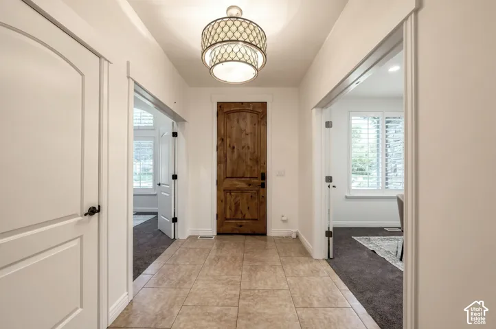 Entryway featuring a rustic wood-finish front door, large-format tile flooring, a tiered drum-style pendant light fixture, and arched-panel interior doors with matte black hardware