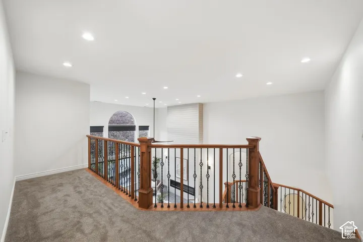 Landing area featuring carpeted flooring, recessed lighting, and a prominent wooden railing with metal balusters