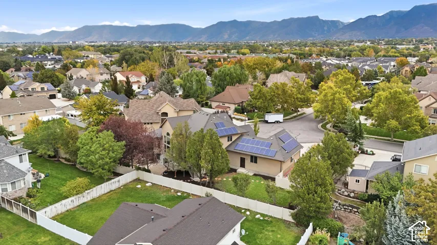 Aerial view featuring a multi-level residence with installed rooftop solar panels, a fenced backyard, and surrounding mountain scenery