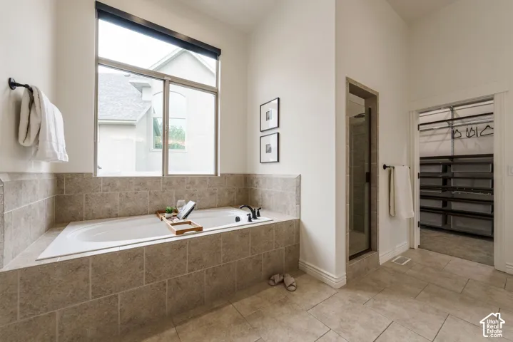 Soaking tub with tile surround, glass-enclosed shower, built-in storage shelving, and large-format tile flooring