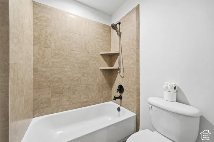 Bathtub featuring tan stone-finish tile surround, integrated corner shelving, and matte black plumbing fixtures