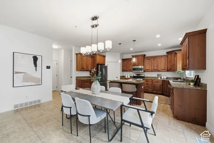 Kitchen featuring rich-toned wood cabinetry, stone countertops, stainless steel appliances, tile flooring, and a multi-light chandelier