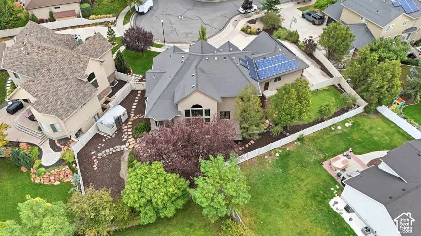 Aerial perspective featuring a multi-gabled roofline, integrated solar panel array, fenced backyard, mature trees, and a flagstone pathway