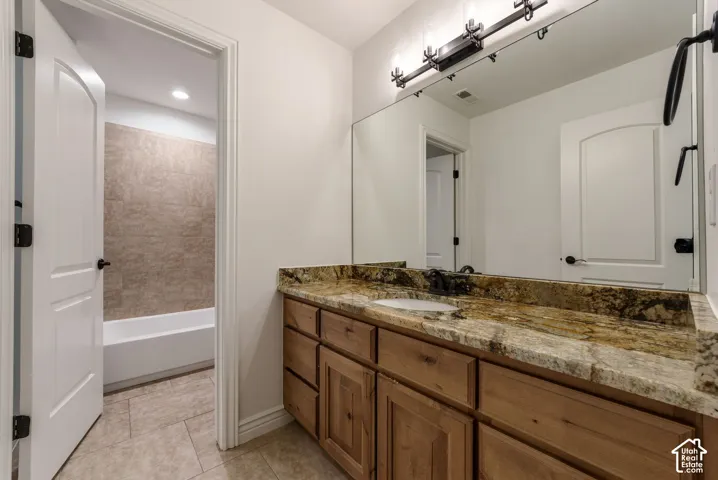 Bathroom vanity featuring wood cabinetry, stone-finish countertop, undermount sink, and large wall-mounted mirror with multi-light fixture