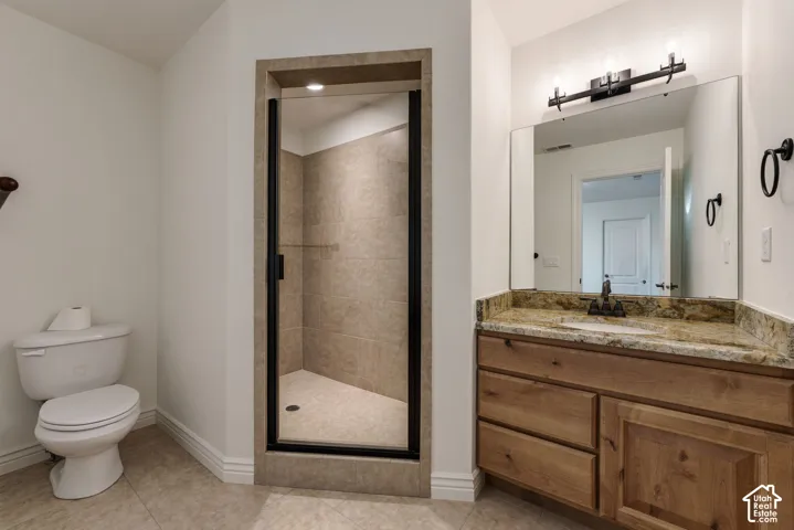 Bathroom featuring a wood vanity with stone-surfaced countertop, integrated sink, tiled walk-in shower with matte black frame, and wall-mounted vanity lighting