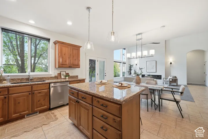 Kitchen featuring wood cabinetry, stone-surface countertops, central island, dual pendant lighting, and tile flooring