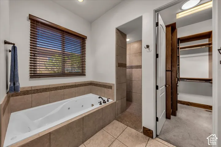Jetted soaking tub with tile surround, walk-in shower with tiled walls and flooring, and wood-finish window blinds