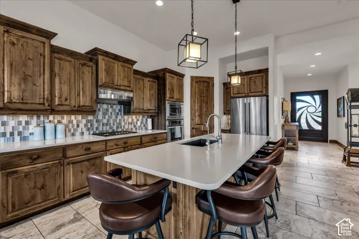 Kitchen featuring wood cabinetry, stainless steel appliances, a white island countertop with an undermount sink, and pendant lighting