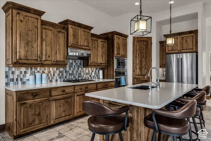 Kitchen featuring extensive wood cabinetry, a large kitchen island with seating, a mosaic tile backsplash, built-in stainless steel appliances, and tile flooring