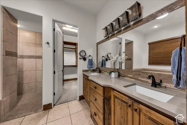 Double vanity with integrated sinks, stone-finish countertops, wood-finish cabinetry, and a tile backsplash