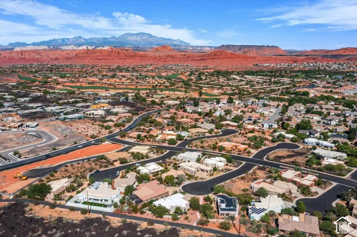 Expansive residential development with winding roads and desert landscaping, set against a backdrop of red rock formations and distant mountains