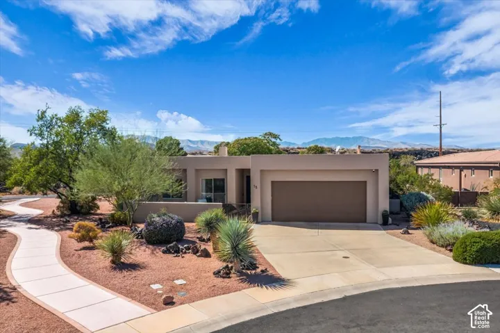 Stucco exterior, attached two-car garage, concrete driveway, front desert landscaping, and a winding concrete pathway