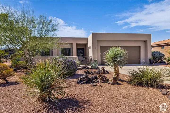 Contemporary stucco exterior with a flat roofline, integrated garage, and a desert-adapted landscape design featuring mature plants and decorative rock