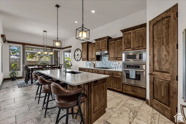 Spacious kitchen featuring wood-finish cabinetry, stainless steel appliances, a center island with a sink, and tile flooring