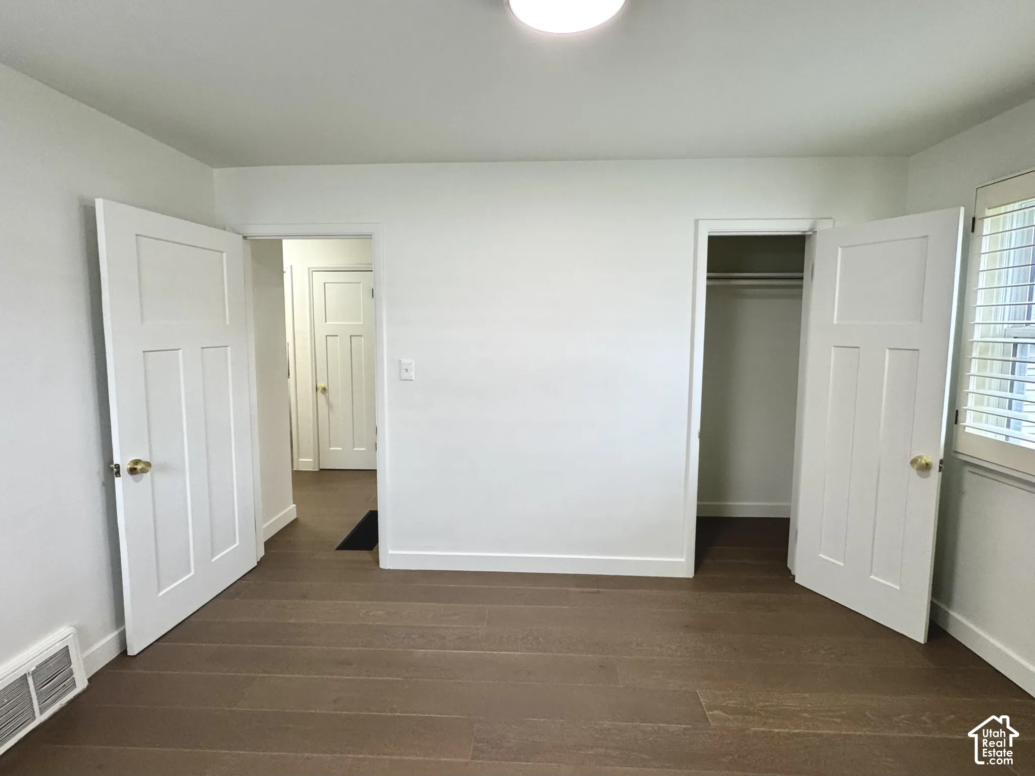 Primary bedroom with real wood flooring, white paneled doors, and window plantation shutters