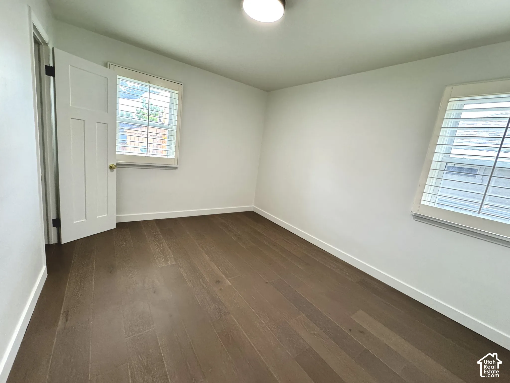 Primary bedroom with real wood flooring, white paneled doors, and window plantation shutters