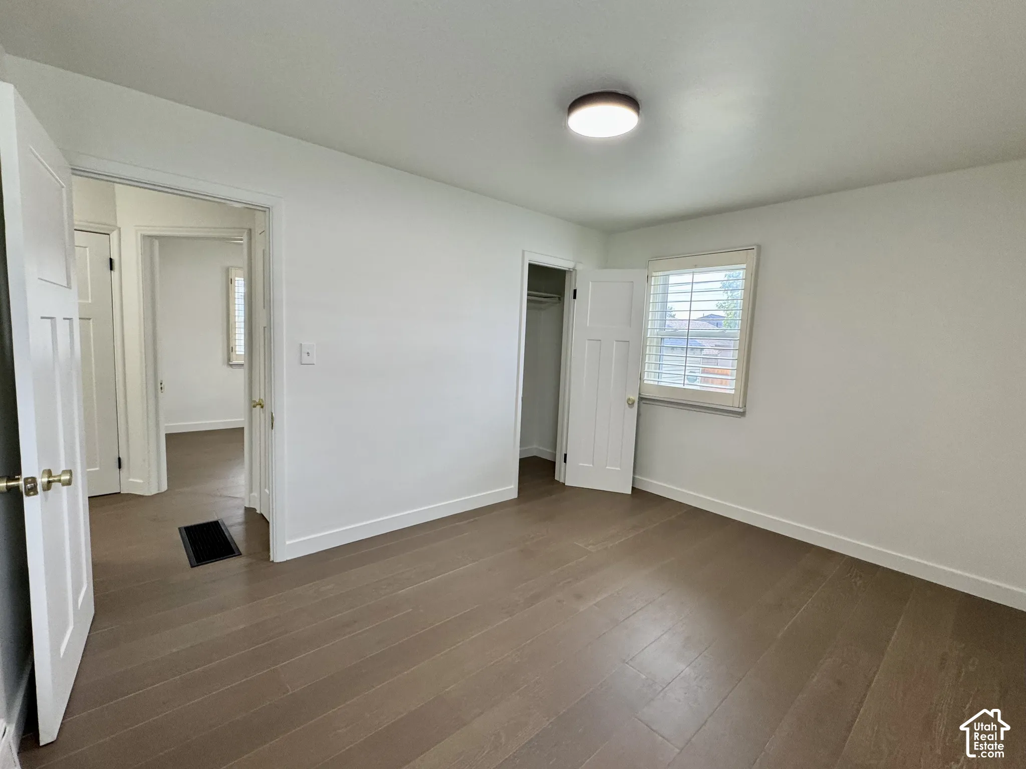 Primary bedroom with real wood flooring, white paneled doors, and window plantation shutters