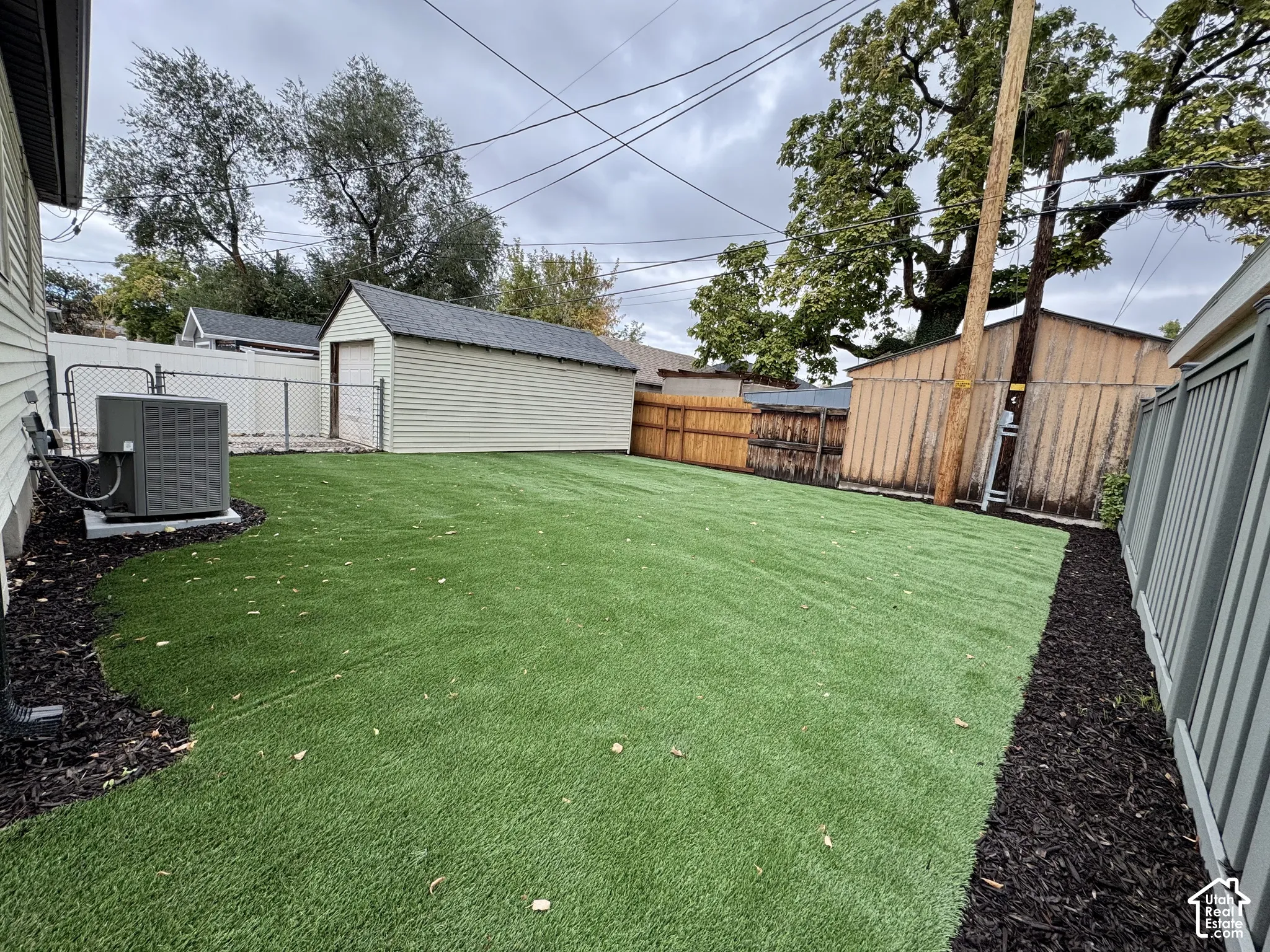 Backyard featuring synthetic turf, mulch perimeter, detached garage, and perimeter fencing