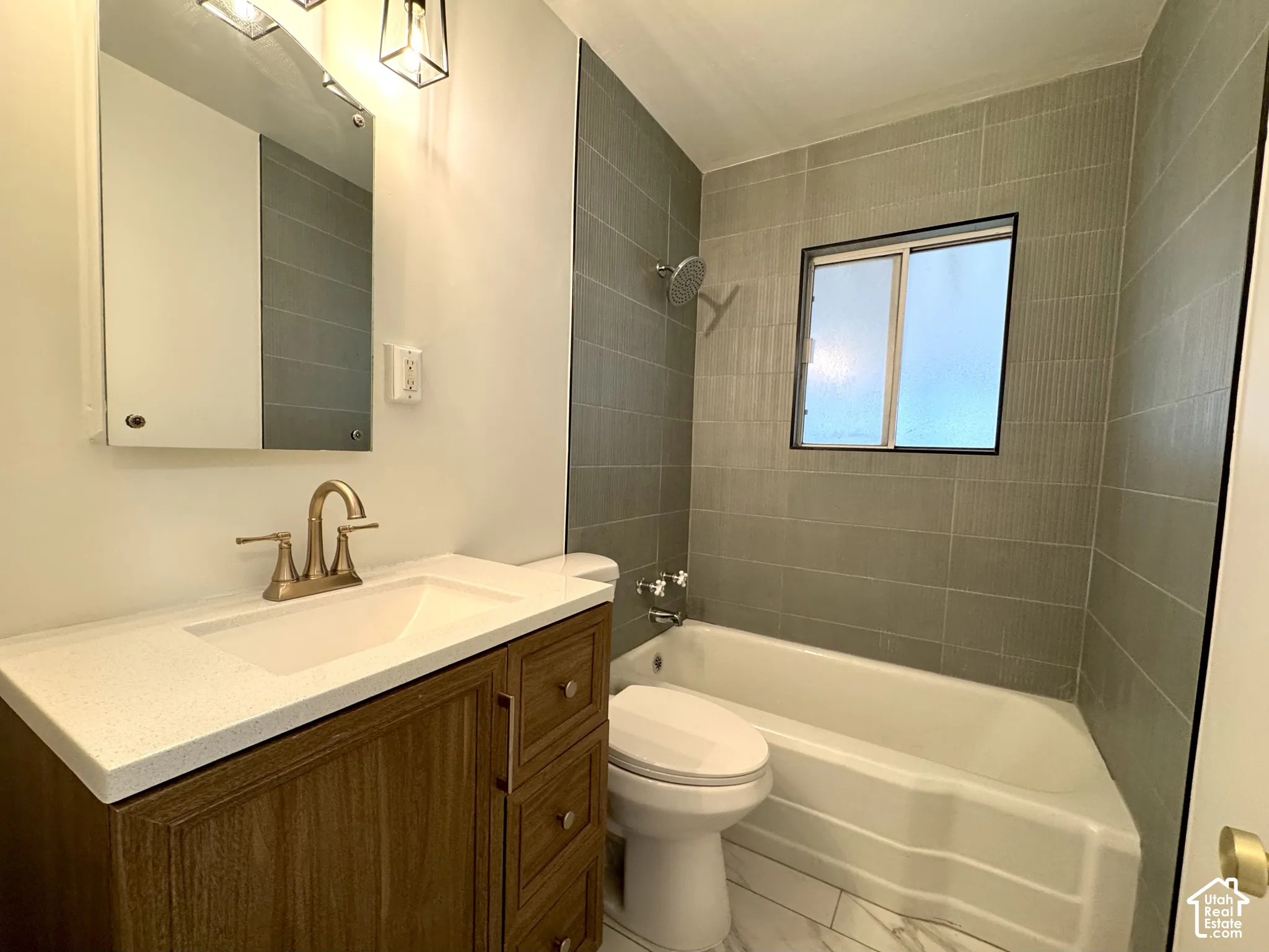 Bathroom featuring a wood-finish vanity with a light-toned countertop, a tub-shower combination with full-height green tile surround, and polished metal fixtures with tile flooring.