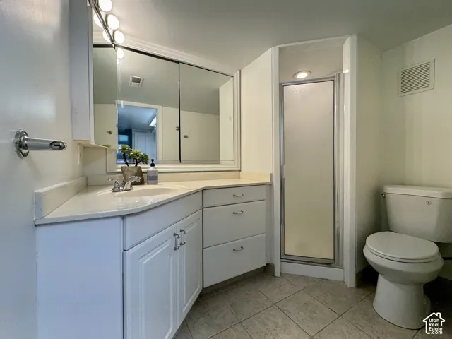 Bathroom featuring white cabinetry, solid-surface countertop with an integrated sink, large mirrored medicine cabinet, enclosed shower stall, and tiled flooring