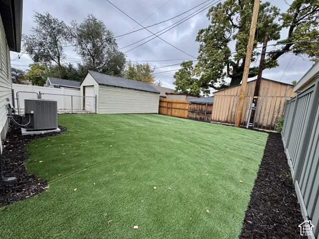 Backyard featuring synthetic turf, mulch perimeter, detached garage, and perimeter fencing