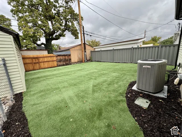 Fenced backyard featuring synthetic turf, dark mulch landscaping, and an exterior HVAC unit