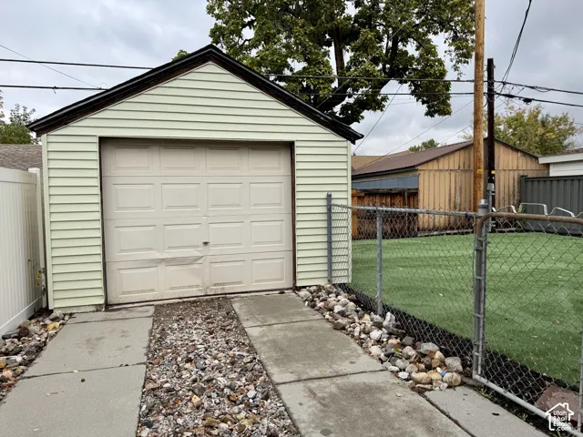 Detached garage featuring light-colored horizontal siding, a single-bay sectional door, concrete driveway, and chain-link perimeter fencing