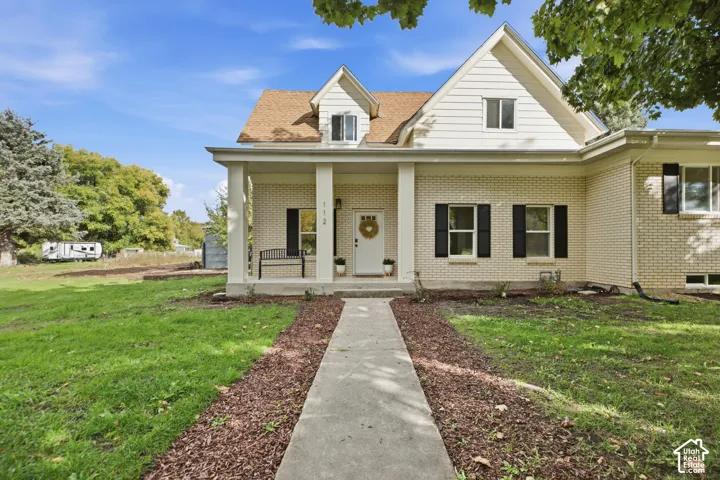 Exterior facade featuring light-colored brick siding, a covered front porch with square columns, gabled rooflines, and contrasting black shutters