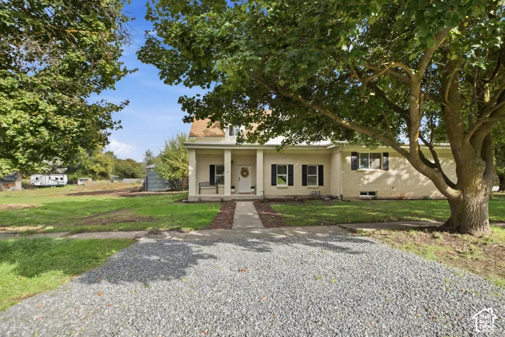 Brick exterior featuring a covered front porch, dark-toned shutters, and a gravel driveway