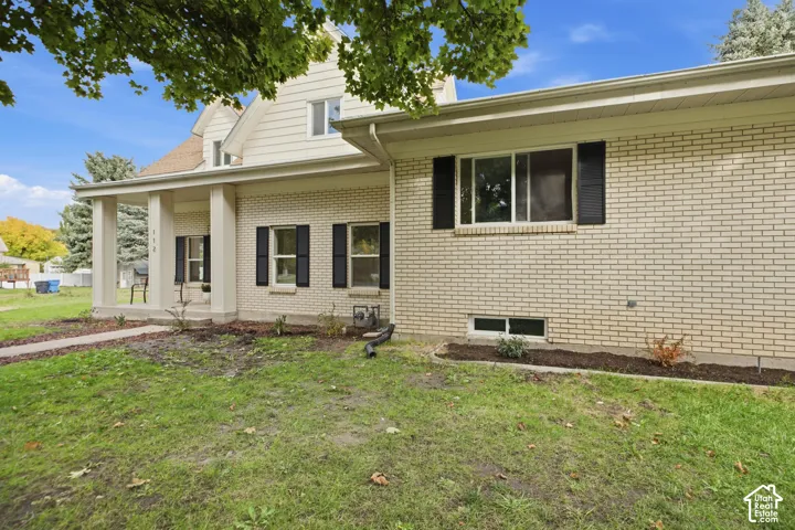 Exterior featuring cream-colored brick masonry, dark window shutters, a covered front porch with square columns, and horizontal siding on the upper level