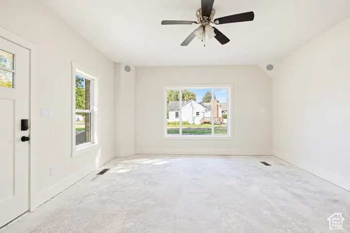 Neutral interior space featuring crisp white walls, a large picture window, a classic multi-light exterior door, and a central ceiling fan with an integrated light fixture