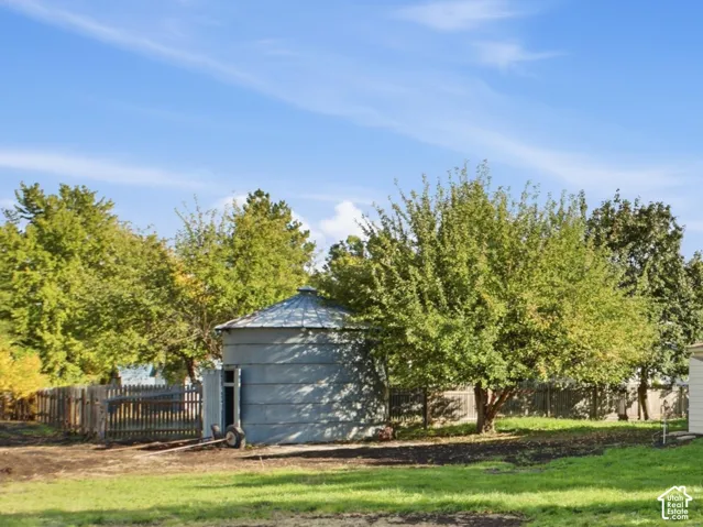 Two-story residence featuring light-colored horizontal siding, a covered front porch with square columns, gabled rooflines, and a detached metal grain bin situated on a parcel with mature trees