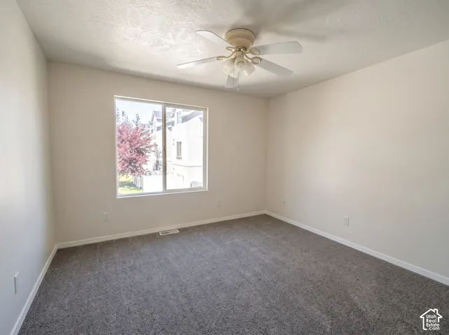 Room featuring neutral wall tones, gray carpeting, a multi-blade ceiling fan with integrated lighting, and a large sliding window