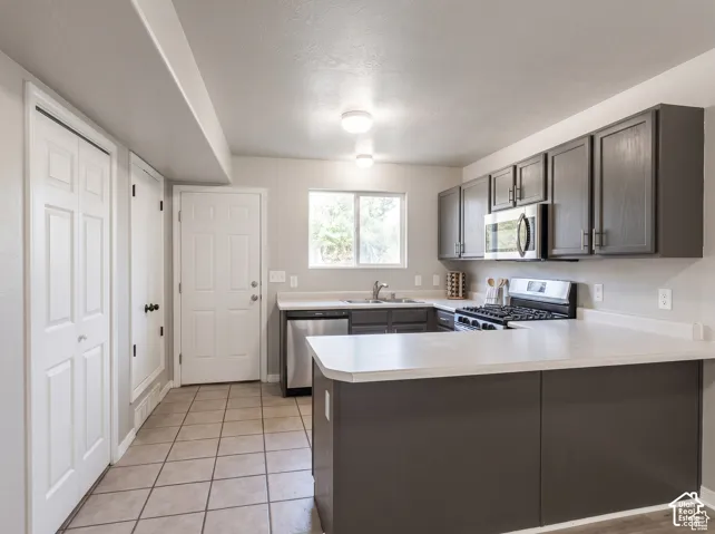 Kitchen featuring dark-toned cabinetry, stainless steel appliances, solid-surface countertops, tile flooring, and dual-closet storage