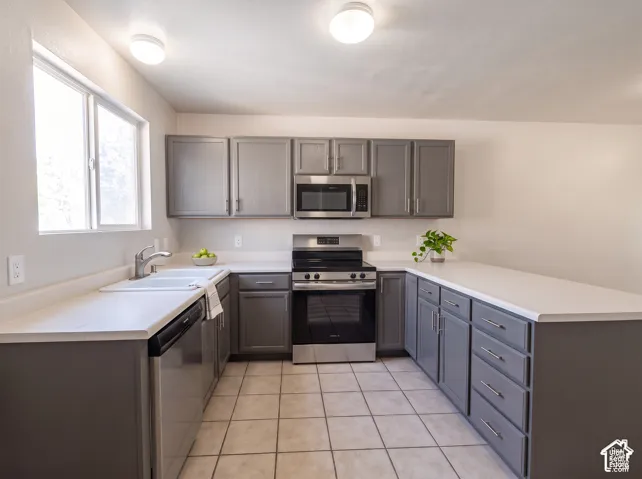 Kitchen featuring grey shaker-style cabinetry, solid-surface countertops, tile flooring, and stainless steel appliances