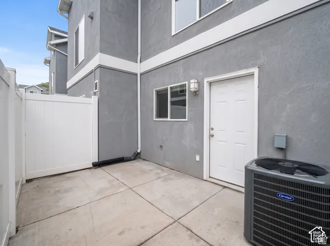 Concrete patio featuring a white vinyl privacy fence, exterior door, and wall-mounted light fixture