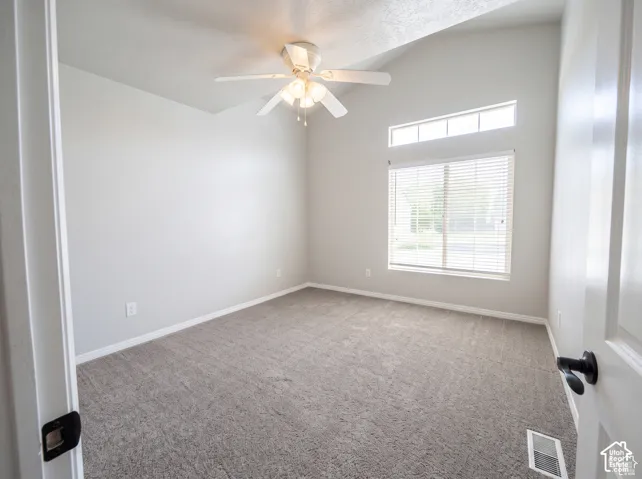 Vaulted ceilings, neutral carpeting, transom window, and a ceiling fan with integrated lighting