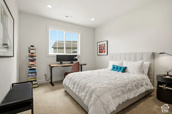 Recessed lighting, large window, neutral wall paint, light-toned carpeting, and a fabric-upholstered headboard