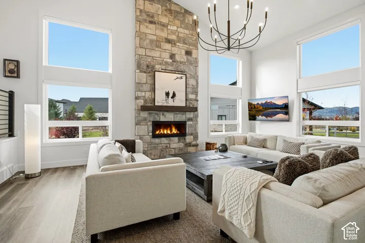 Two-story stone-clad fireplace with an integrated linear firebox and wood mantel, wood-finish flooring, high ceilings, multiple large windows, and a multi-arm chandelier